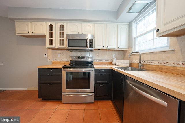 kitchen featuring wood counters, sink, light tile patterned floors, appliances with stainless steel finishes, and white cabinetry