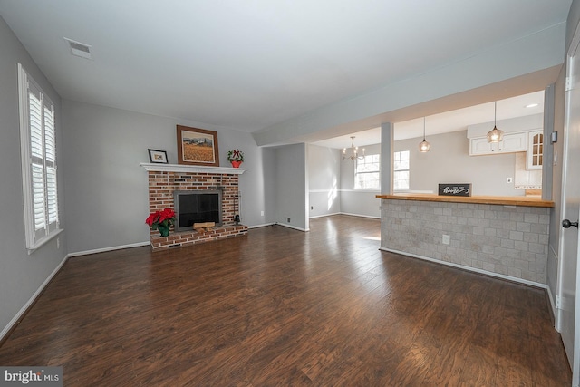 unfurnished living room featuring dark wood-type flooring, a healthy amount of sunlight, a notable chandelier, and a brick fireplace