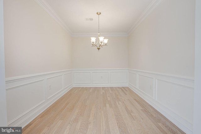 unfurnished room with light wood-type flooring, a notable chandelier, and ornamental molding