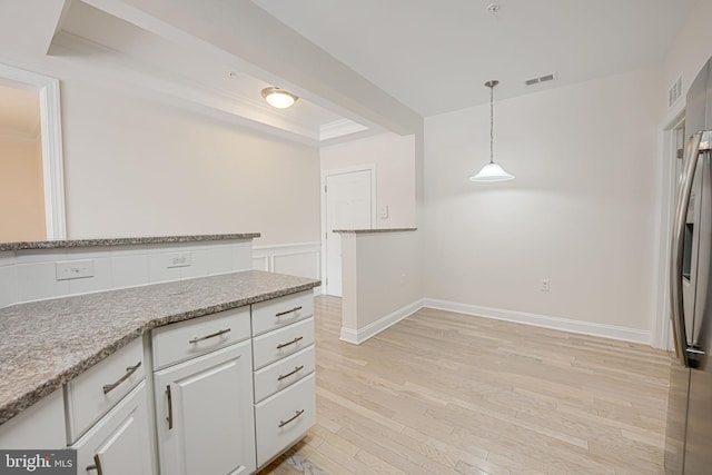 kitchen with a raised ceiling, decorative light fixtures, white cabinets, light wood-type flooring, and light stone counters