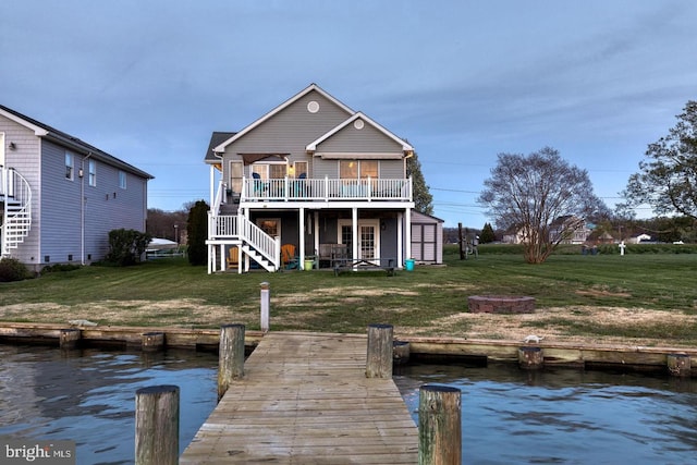 back of house with a deck with water view, a fire pit, and a lawn