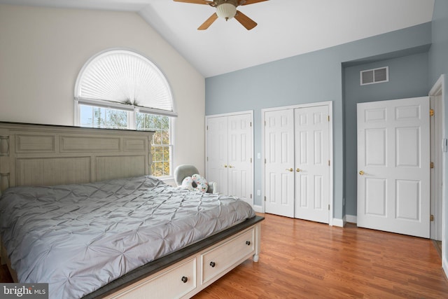 bedroom featuring multiple closets, light hardwood / wood-style floors, ceiling fan, and lofted ceiling