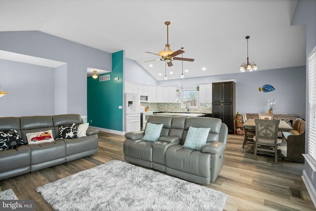 living room with ceiling fan with notable chandelier, lofted ceiling, sink, and light hardwood / wood-style flooring