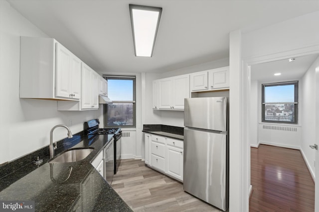 kitchen featuring dark stone countertops, light hardwood / wood-style flooring, white cabinets, and appliances with stainless steel finishes