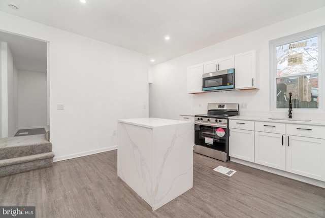 kitchen featuring white cabinetry, sink, a center island, light hardwood / wood-style floors, and appliances with stainless steel finishes