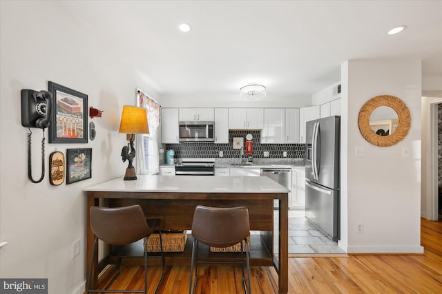 kitchen featuring white cabinetry, kitchen peninsula, a kitchen bar, decorative backsplash, and appliances with stainless steel finishes