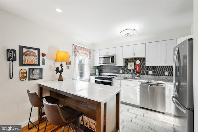 kitchen with kitchen peninsula, appliances with stainless steel finishes, a breakfast bar, sink, and white cabinets