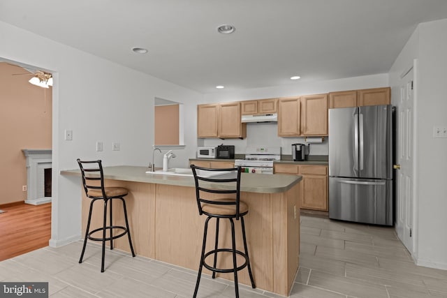 kitchen featuring kitchen peninsula, white appliances, ceiling fan, sink, and a breakfast bar area