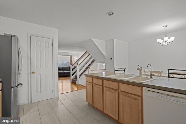 kitchen featuring stainless steel refrigerator, sink, an inviting chandelier, white dishwasher, and decorative light fixtures