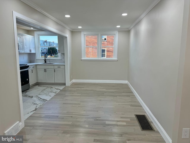 interior space with backsplash, electric range oven, ornamental molding, sink, and white cabinetry