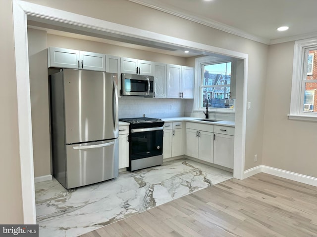 kitchen with appliances with stainless steel finishes, ornamental molding, sink, light hardwood / wood-style flooring, and white cabinetry