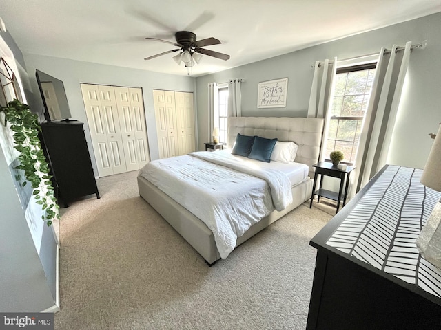 bedroom featuring ceiling fan, light carpet, and two closets