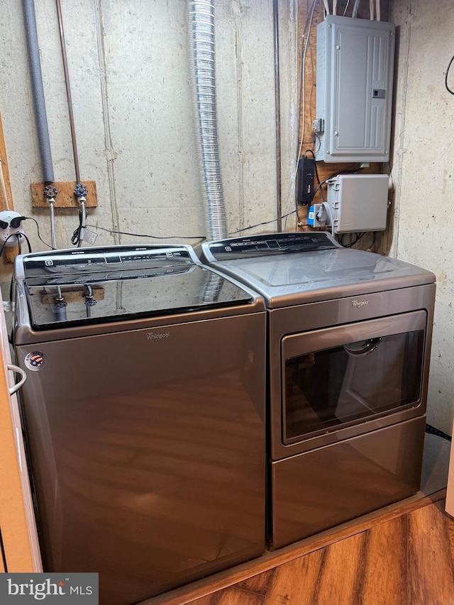 clothes washing area with electric panel, washer and clothes dryer, and hardwood / wood-style flooring