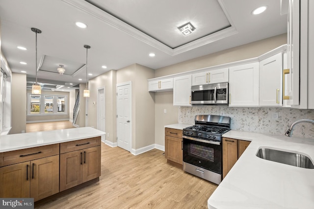 kitchen featuring appliances with stainless steel finishes, sink, pendant lighting, light hardwood / wood-style flooring, and white cabinetry