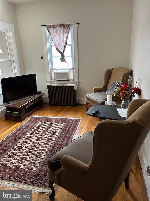 living area with radiator heating unit, cooling unit, and wood-type flooring