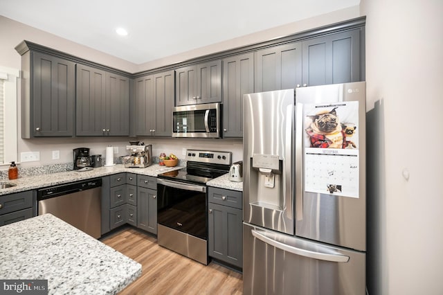 kitchen featuring light wood-type flooring, stainless steel appliances, light stone counters, and gray cabinetry