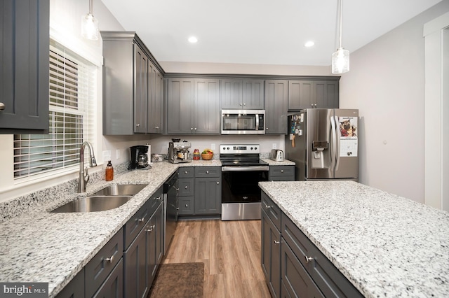 kitchen with appliances with stainless steel finishes, light hardwood / wood-style floors, pendant lighting, and sink