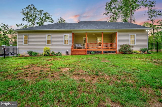 back house at dusk with ceiling fan, a wooden deck, and a lawn