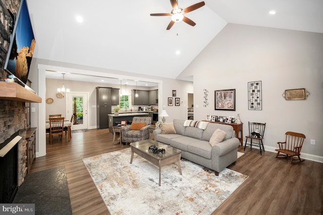 living room with a stone fireplace, dark hardwood / wood-style flooring, high vaulted ceiling, and ceiling fan with notable chandelier