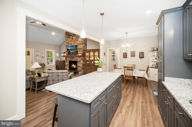 kitchen featuring a fireplace, decorative light fixtures, light hardwood / wood-style floors, and vaulted ceiling