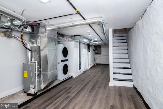 basement featuring heating unit, stacked washer / dryer, electric panel, and dark wood-type flooring