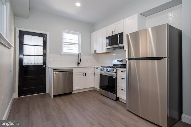 kitchen with white cabinets, backsplash, stainless steel appliances, and light hardwood / wood-style flooring