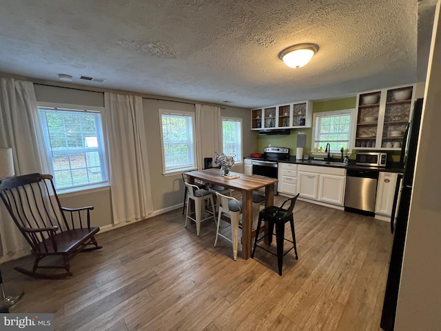 kitchen featuring hardwood / wood-style flooring, white cabinetry, a textured ceiling, and appliances with stainless steel finishes