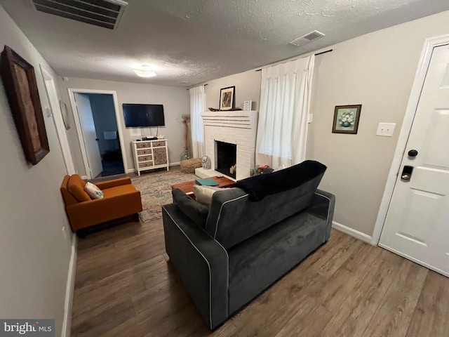 living room featuring a textured ceiling, hardwood / wood-style flooring, and a brick fireplace