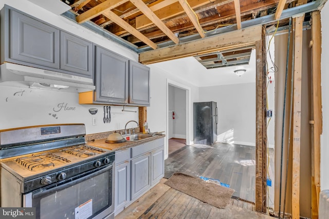 kitchen with gray cabinetry, sink, stainless steel gas range oven, light hardwood / wood-style floors, and black refrigerator