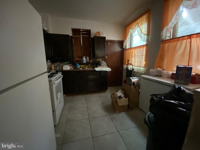 kitchen with dark brown cabinetry, light tile patterned flooring, and white appliances