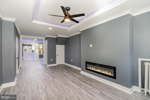 unfurnished living room featuring a raised ceiling, ceiling fan, light hardwood / wood-style flooring, and ornamental molding