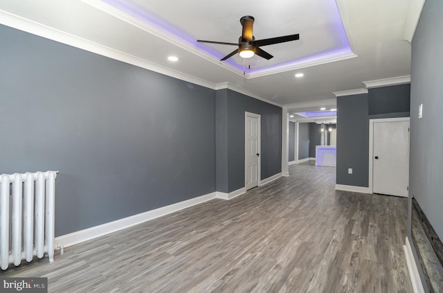 empty room with radiator heating unit, ceiling fan, ornamental molding, a tray ceiling, and wood-type flooring