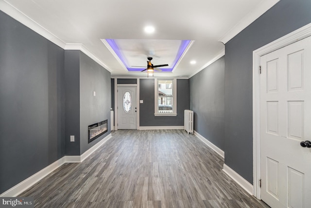 entrance foyer with crown molding, ceiling fan, dark hardwood / wood-style floors, a tray ceiling, and radiator heating unit