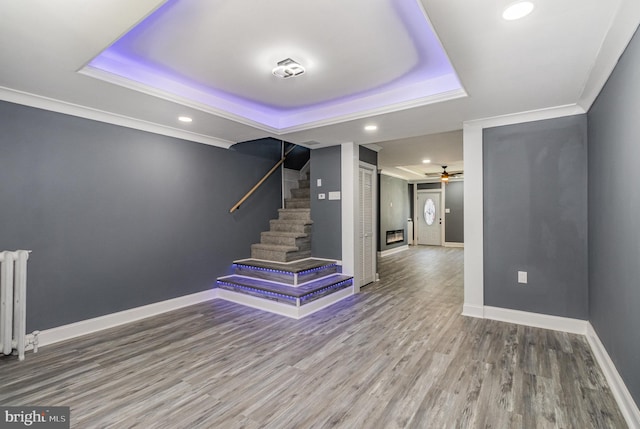 staircase with a tray ceiling, ceiling fan, crown molding, hardwood / wood-style floors, and radiator heating unit