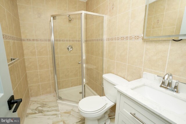 bathroom with vanity, toilet, a shower with door, and tile walls