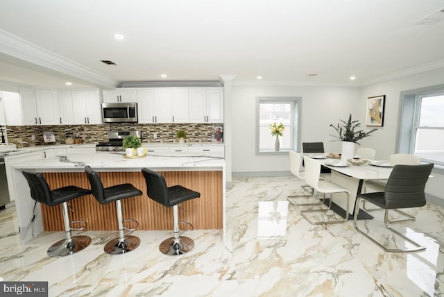 kitchen featuring white cabinets, a spacious island, a breakfast bar area, ornamental molding, and stainless steel appliances