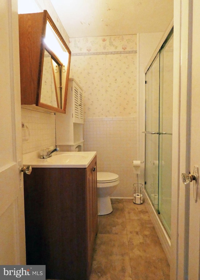 bathroom with toilet, vanity, tile walls, and walk in shower