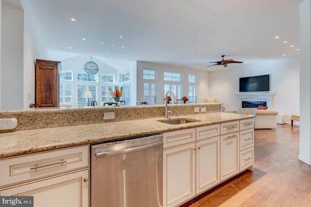 kitchen with sink, stainless steel dishwasher, ceiling fan, light stone countertops, and light hardwood / wood-style floors