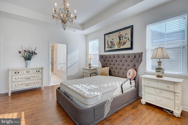 bedroom with ensuite bath, a tray ceiling, dark hardwood / wood-style flooring, and a chandelier