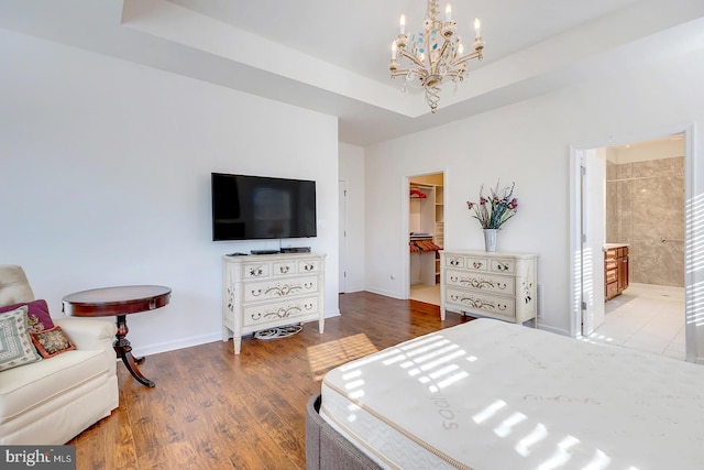 bedroom with hardwood / wood-style floors, a raised ceiling, a spacious closet, a closet, and a chandelier