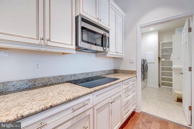 kitchen with light hardwood / wood-style flooring, light stone countertops, white cabinets, washing machine and clothes dryer, and black electric cooktop