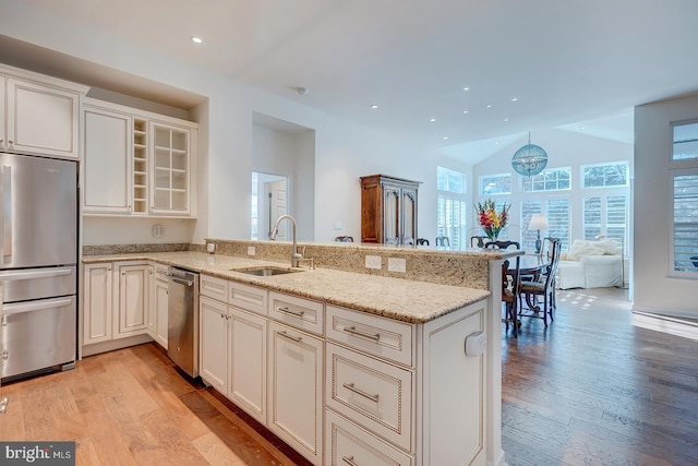 kitchen with sink, stainless steel refrigerator, light stone countertops, kitchen peninsula, and light wood-type flooring