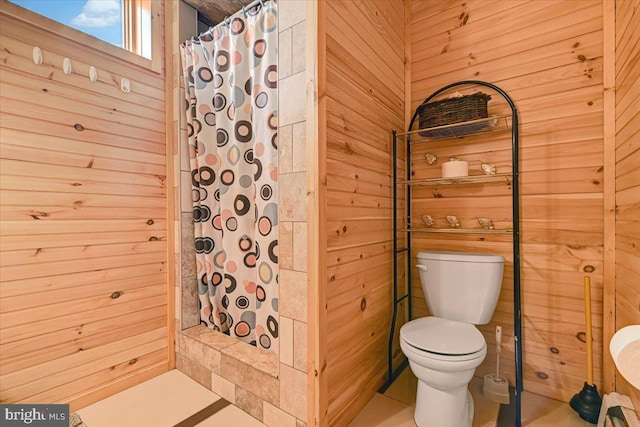 bathroom with tile patterned flooring, toilet, walk in shower, and wooden walls