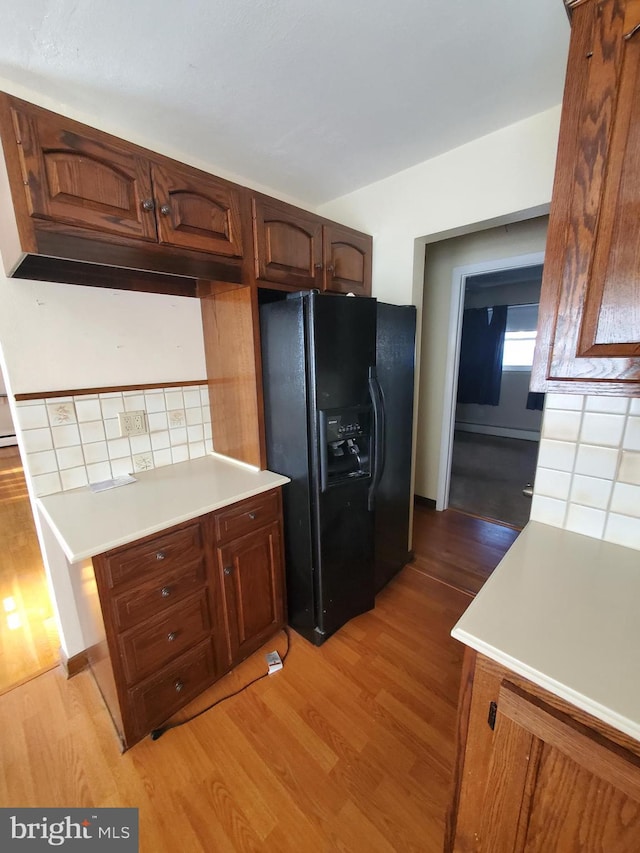 kitchen with tasteful backsplash, light hardwood / wood-style flooring, and black refrigerator with ice dispenser