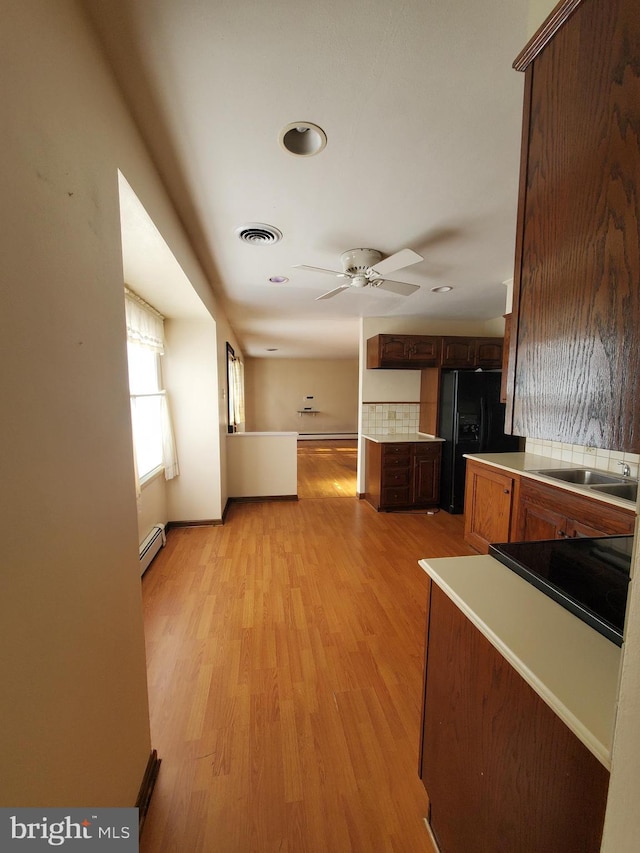 kitchen with a baseboard radiator, sink, ceiling fan, black fridge with ice dispenser, and light hardwood / wood-style floors