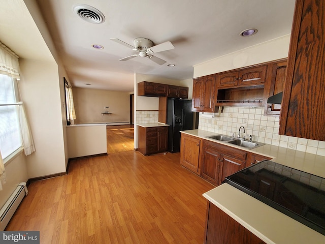 kitchen with sink, light hardwood / wood-style flooring, black refrigerator with ice dispenser, backsplash, and a baseboard radiator