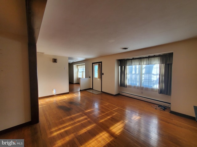 unfurnished room with a baseboard heating unit and hardwood / wood-style floors