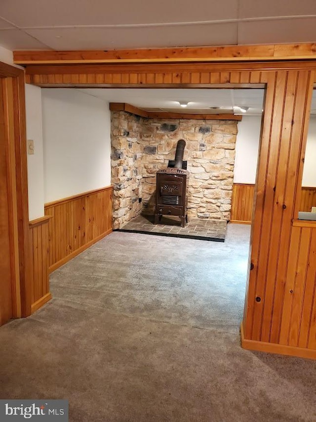 unfurnished living room featuring wooden walls, carpet floors, and a wood stove