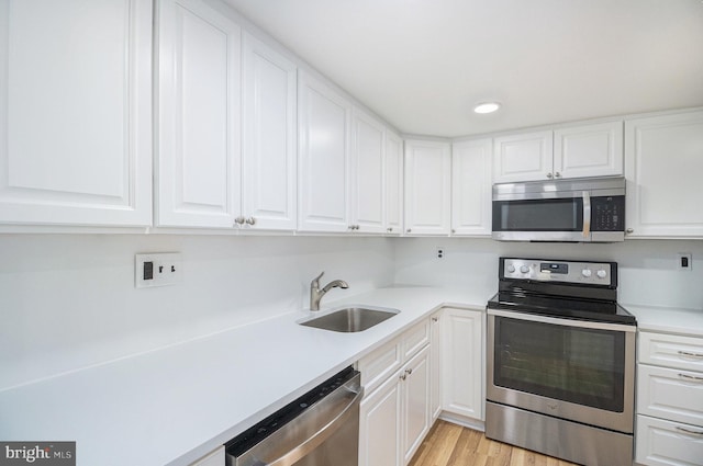 kitchen featuring appliances with stainless steel finishes, light hardwood / wood-style flooring, white cabinetry, and sink