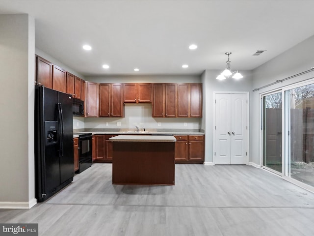 kitchen with sink, decorative light fixtures, a kitchen island, black appliances, and light wood-type flooring